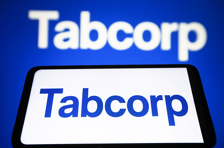 In this photo illustration, Tabcorp logo is seen on a smartphone and a pc screen.