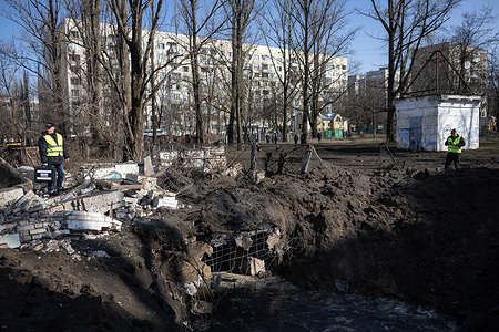 Utility workers stand near the crater left by a Russian missile explosion near residential buildings in Kyiv. According to the State Emergency Service of Ukraine, rockets hit three districts of the Ukrainian capital on the morning of March 21, damaging residential buildings and injuring at least 10 people.
