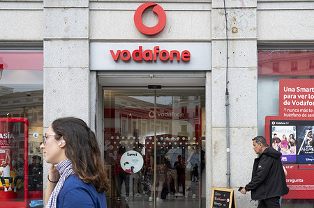 Pedestrians walk past a British multinational telecommunications corporation and phone operator, Vodafone, store in Spain.