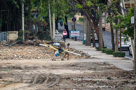 A female waste picker is seen leaving a cleared land with a supermarket cart full of collected garbage, including water and electric plastic pipes, on Lat Phrao Road, in Bangkok. Bangkok's waste pickers or salengs, mostly elderly, play a vital role in the city's circular economy by collecting street trash. Despite their contribution, they suffer poverty, insecurity, health risks, and stigma.