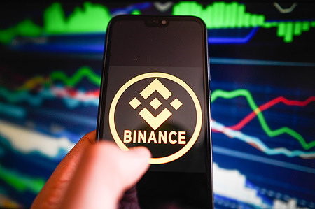 In this photo illustration, a Binance logo is displayed on a smartphone with stock market percentages in the background.