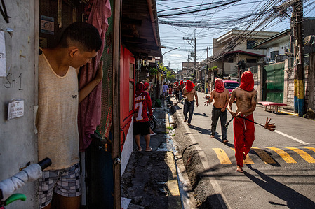 A man watches Filipino flagellants walk along a street in Mandaluyong City. Many Filipino Catholic devotees observe Holy Week by engaging in various forms of physical penance, including self-flagellation, as a means of repentance for their sins.