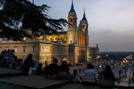 A group of young people wait for the sunset in front of the Almudena Cathedral in Madrid.