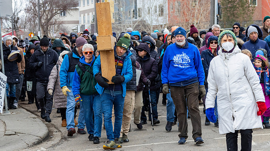 A participant carries a wooden cross as hundreds of devotees follow in the Way of the Cross procession through downtown Edmonton. The Way of the Cross procession is a symbolic reenactment and commemoration of Jesus’s journey to the place of his crucifixion on Mount Golgotha. Participants take turns to carry the cross as an expression of their faith.