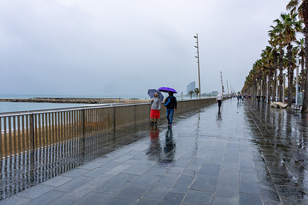 A couple walks along Barceloneta and protects themselves from the rain with an umbrella during the Storm Nelson. View of Barceloneta Beach in Barcelona, Spain, during Storm Nelson, which has prompted yellow alerts in ten Spanish communities during this Holy Week due to rain, wind, or snow.