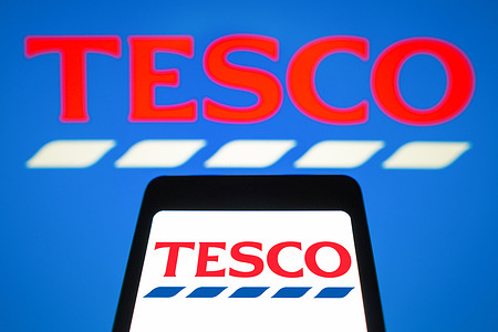 In this photo illustration, the Tesco logo is displayed on a smartphone screen and in the background.