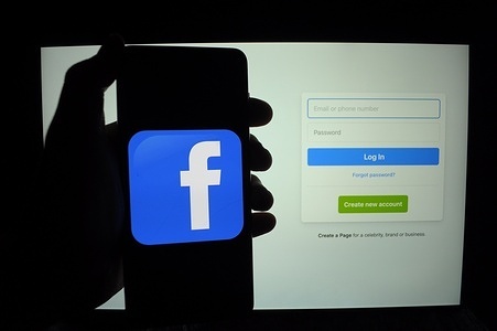 In this photo illustration, the Facebook logo is seen on a smartphone screen, which is in front of the Facebook log-in page on a laptop screen.
