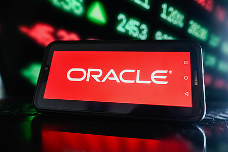 In this photo illustration, an Oracle logo is displayed on a smartphone with stock market percentages in the background.