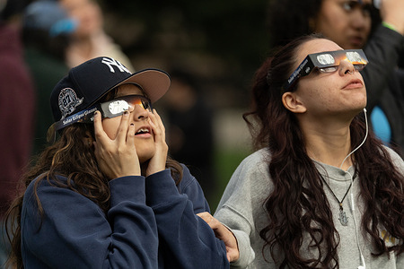 A woman presses her special viewing glasses against her face to block out light pollution to catch a glimpse of the 2024 Solar Eclipse from Central Park.