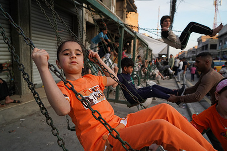 Iraqi children play on a swing at a mobile amusement park as they celebrate Eid al-Fitr which marks the end of the Muslim holy fasting month of Ramadan, in the old city of Mosul, northern Iraq