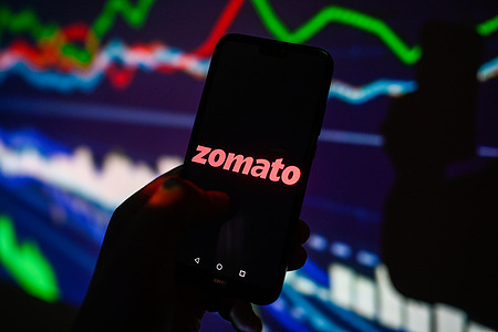 In this photo illustration, a Zomato logo is displayed on a smartphone with stock market percentages on the background.