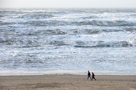 People are seen walking at the beach during stormy weather. Zandvoort is located on the North Sea in Netherlands. The town is considered one of the biggest beach resorts in the country. its long sandy beaches and coastal dunes attract tourists from all over the Netherlands and abroad during the warm summer months.