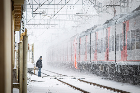 A man stands at a railway crossing near a passing train during heavy snowfall in St. Petersburg.