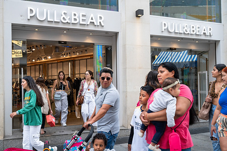 Shoppers and pedestrians walk past a Spanish multinational clothing design retail company Inditex, Pull & Bear (Pull&Bear), store and logo in Spain.