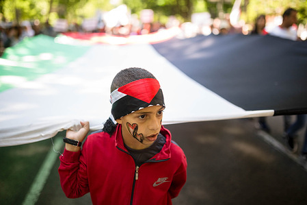 A young boy holds a giant Palestinian flag during a demonstration in solidarity with the Palestinian people. Protesters march around the main streets of Madrid, under the slogan "Let's stop the genocide in Palestine", demanding the Spanish government stop the arms trade with Israel.