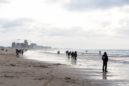 People are seen walking at the seaside in Oostende (Ostend). Oostende is a coastal city located in the western part of Belgium, on the North Sea. The city has a beautiful long beach and is a popular destination for many tourists.