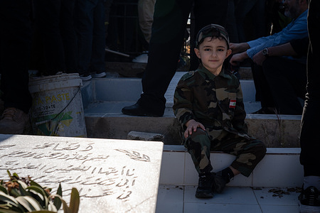 A boy dressed in military patterned uniform with a Lebanese patch sits in front of a grave during a funeral of Hezbollah fighter in Mansouri. Hezbollah held a funeral in southern Lebanon for its fighters who were killed in an Israeli strike. Israeli forces and the Lebanese group Hezbollah have intensified its cross-border fighting, raising fears of an escalation as Israel continues its war on Gaza and after Iran and Israel exchanged fire.
