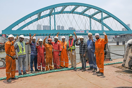 Construction workers flash a victory sign as they pose for a photo in front of bow string arch bridge connecting coastal road to Bandra Worli sealink installed at the Worli (area in South Mumbai) end in Mumbai.