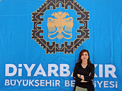 Diyarbakir Metropolitan Municipality Co-Mayor Ayşe Serra Bucak is seen in front of the municipality emblem. In Turkey, investigations initiated by the Ministry of Internal Affairs and Prosecutors' Offices regarding the allegations that the Turkish flag was raised in the municipal buildings and the Turkish national anthem was not sung about the Diyarbakir and Mardin Metropolitan Municipalities, which were won by the Kurdish opposition, and the Municipality of Diyarbakır's Sur district, continue. The allegations and some images were published on social media accounts. Inspectors from the Ministry of Internal Affairs came to Diyarbakir and started working. The mayors of the three municipalities said that such a situation did not occur, that the published photos were a montage and that they were faced with a perception provocation. After this short statement, the presidents decided not to talk about this issue in order not to create polemics.