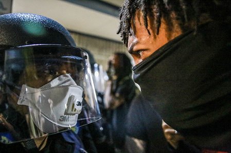 A protester stands face to face with a police officer during the demonstration.A peaceful protest, spurred by the death of George Floyd, turned violent as protesters clashed with police, throwing rocks and bottles at police while police responded by shooting pepper spray balls at protesters and using flash bang grenades to disperse the crowd.