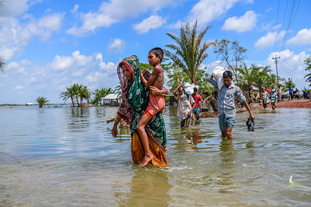 People crossing the broken flooded road after the landfall of cyclone Amphan during the aftermath.Thousands of shrimp enclosures have been washed away, while numerous thatched houses, trees, electricity and telephone poles, dykes and croplands were damaged and many villages were submerged by the tidal surge of the Amphan at Assasuni, in Satkhira District.