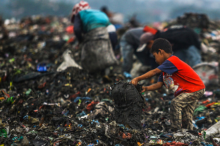 A child of a scavenger community, helps his parents who work as scavengers sort through a pile of garbage for recycling.