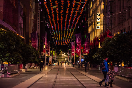 A night view of Bourke Street Mall with Christmas decorations above tram tracks and few people are out.