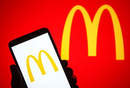In this photo illustration a McDonald's logo is seen on a smartphone in a hand and a pc screen.