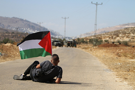 A Palestinian protester laying in the road holding a Palestinian flag in front of Israeli soldiers during a demonstration against Israeli settlements in the village of Beit Dajan near the West Bank city of Nablus.