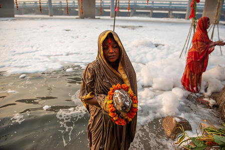 A married woman standing in the toxic river which is full of hazardous foam to pray to the Sun god with some offerings, during the festival.
Chhath Puja is a significant festival in northern India, primarily celebrated in Bihar, Jharkhand, east Uttar Pradesh, and some parts of Nepal. Devotees worship Surya Dev (Sun) during these days. The white toxic foam and Hazardous float and cover the Yamuna river which is caused by increased ammonia levels and high phosphate content in water.