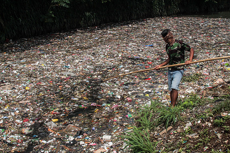 A man nets plastic waste to let water flow in the Bojong Citepus River which empties into the Citarum River in Dayeuhkolot.The National Plastic Action Partnership (NPAP) notes that there are about 4.8 million tons per year of plastic waste in Indonesia is not well managed such as being burned in open spaces (48%), unmanageable in official landfills (13%) and the rest polluting waterways and seas (9%).