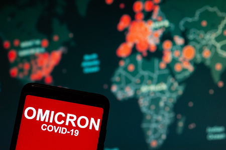 In this photo illustration, a phone screen shows a text that says Omicron COVID-19 in front of a map displaying the location of the worst hit areas of Covid-19