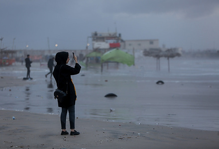 A Palestinian young lady making a video call at the Mediterranean beach on a rainy day.