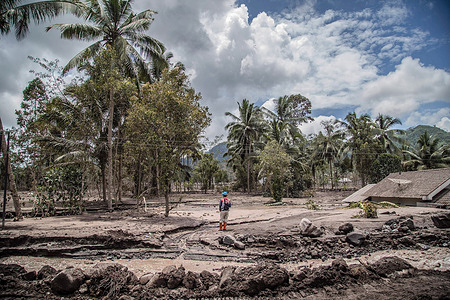 An Indonesian rescue officer stands near trees and a house covered with volcanic ash as he looks for victims in Kamar Kajang villages, Lumajang.At least 14 people are dead and dozens are injured after Mount Semeru, a volcano in Indonesia's East Java province, erupted on Saturday, throwing towers of ash and hot clouds that covered nearby villages.