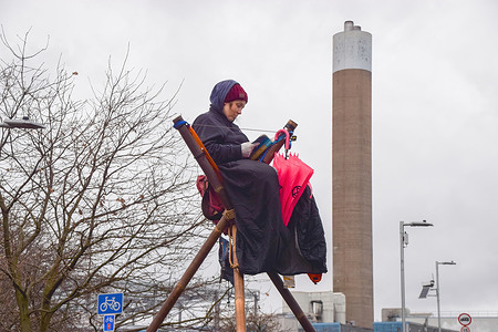 A protester sits and reads a book on a bamboo structure during the demonstration.Extinction Rebellion activists blocked the gates at London Energy with a bamboo structure in protest against the new Edmonton incinerator, which will increase pollution and which the activists call "environmental racism".