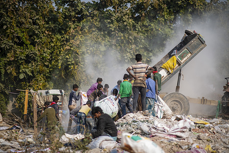 A tractor trailer seen dumping garbage at a landfill site while a group of young rag pickers collect reusable items for livelihood at Cyber City.