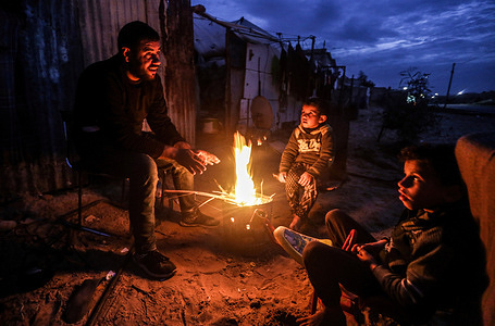 A Palestinian family sits around a fire to warm up in front of their house during the cold weather in the outskirts of Khan Yunis refugee camp.