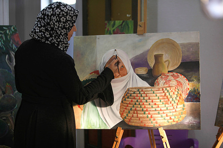 A Palestinian woman painting a traditional Palestinian heritage picture on wooden plank of the olive tree trunks and markets them in the village of Jamaa'in city of Nablus in West Bank.