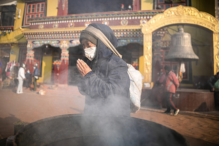A Buddhist devotee offers prayers next to the burning incense at the premises of Boudhanath Stupa in Kathmandu.