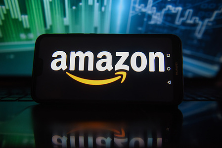 In this photo illustration an Amazon logo is displayed on a smartphone with stock market percentages in the background.