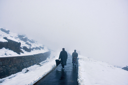 Two Kashmiri men walk along a snow-covered road during a foggy weather in the outskirts of Srinagar.
Moderate to heavy snowfall occurred in the higher areas of Kashmir on Thursday as the weather office forecasted inclement weather until January 9.