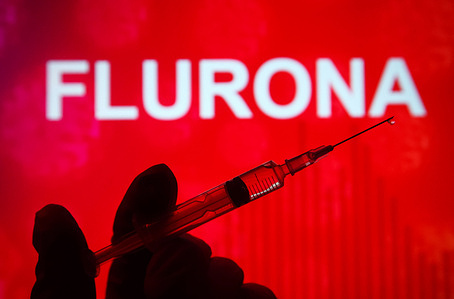 In this photo illustration, a hand holding a medical syringe is seen in front of Flurona word in the background. The media has reported the first case of "Flurona" (Flu+ Coronavirus), a patient with coronavirus disease and flu at the same time.