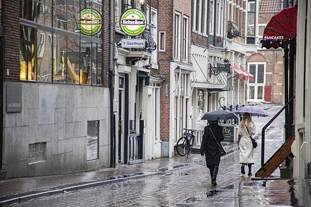 Two ladies holding umbrellas walk in front of a closed bar in the city center.
Daily life in Amsterdam during the 4-week lockdown with the non essential shops, restaurants, cafes, bars, gyms, museums closed.