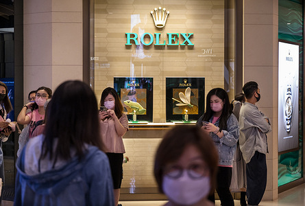 Pedestrians wearing face masks stand in front of the Swiss luxury watchmaker Rolex branch store in Hong Kong.