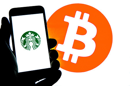 In this photo illustration a Starbucks logo seen displayed on a smartphone with a Bitcoin logo in the background.