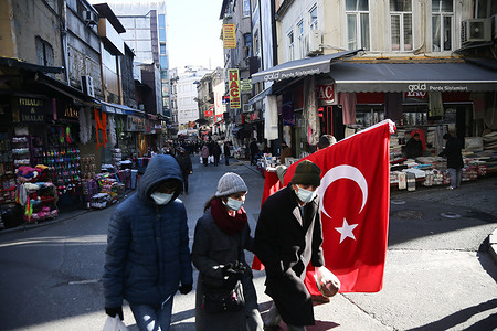 People wearing masks are seen walking past a street vendor selling a Turkish flag.