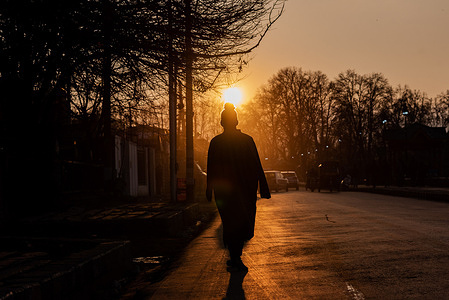 A silhouette of a man walking along the road during sunset.