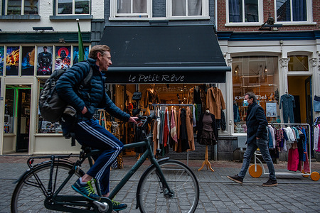 A man seen riding a bicycle, passing by Le Petit Reve clothing store.
Last night, the Dutch government announced a relaxation of the Covid-19 rules for higher education, retail, contact professions, and sports, so this morning non-essentials stores could open again their doors but with some restrictions, the shops may remain open until 5 p.m. and with a maximum number of visitors per square meter. Saturday morning, people flocked in large numbers to shop for the first time since the hard lockdown started earlier in December before Christmas started.