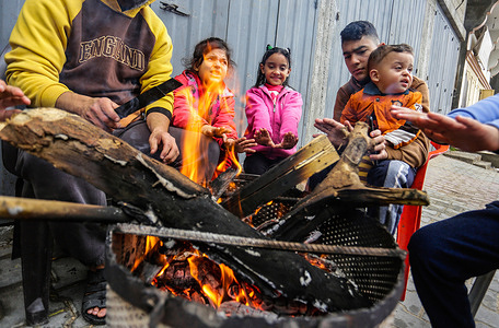 Palestinian refugees seen warming themselves around a street fire amid torrential rain.