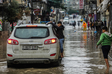 A Palestinian child clings to a moving vehicle to help him get through the flooded street after heavy rain in Jabalia refugee camp in the Northern Gaza Strip.
